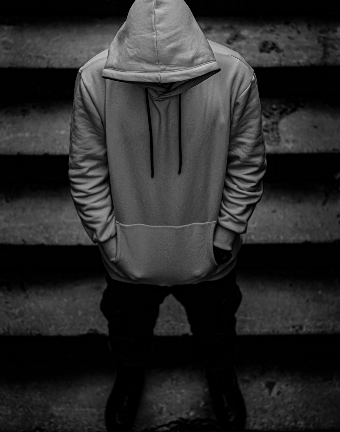 Faceless figure in an oversized hoodie, hands in pockets, standing on concrete steps