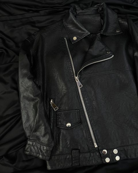 Black leather biker jacket laid flat on black fabric