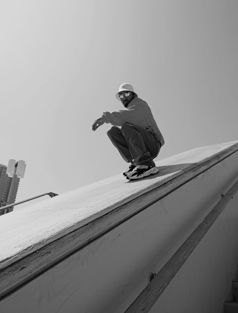 Model crouching on the edge of a sloped rooftop against the sky