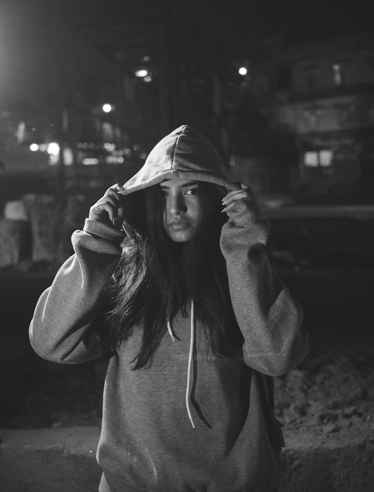 Model pulling up the hood of a gray hoodie on a street at night